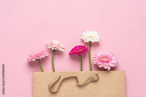 Flowers in craft paper bag on pink background. Pink gerberas. Congratulation gift concept
