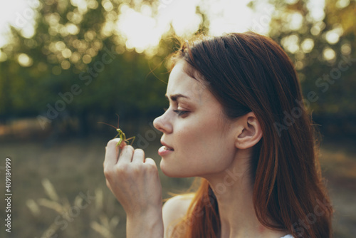 beautiful woman holds a praying mantis on her hand in nature on a meadow in summer