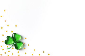 Shamrock symbol made of green decorative glass hearts lying on white background with sparse gold stars confetti. Happy St. Patrick's Day Irish holiday card 17 march lucky clover. Flat lay, copy space