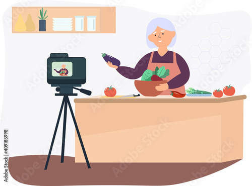 An elderly woman in the kitchen talks about healthy eating. Prepares a dish of vegetables. The concept of writing for a blog, vlog, freelancing, working from home during the period of self-isolation.
