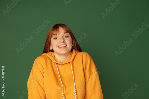 Smiling. Caucasian woman's portrait isolated on green studio background with copyspace. Beautiful female model in yellow sweatshirt. Concept of human emotions, facial expression, sales, ad, fashion. © master1305
