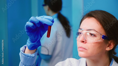 Scientist woman examining blood samples and liquid working in modern equipped laboratory. Team of doctors analysing vaccine evolution using high tech researching diagnosis against covid19