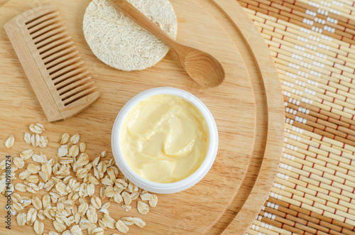 Yellow facial cream (hair mask, body butter) in a small white container and oatmeal. Natural skin and hair concept. Top view, copy space.