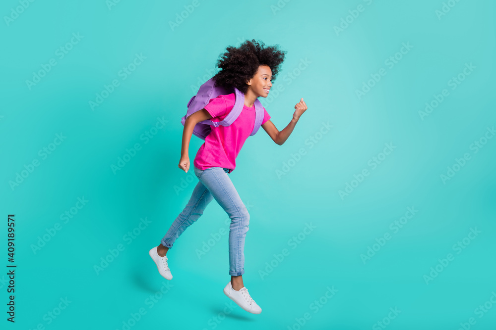Photo portrait full body side profile view of running black skin schoolgirl jumping up isolated on vivid cyan colored background Photo portrait full body side profile view of running black skin schoolgirl jumping up isolated on vivid cyan colored background