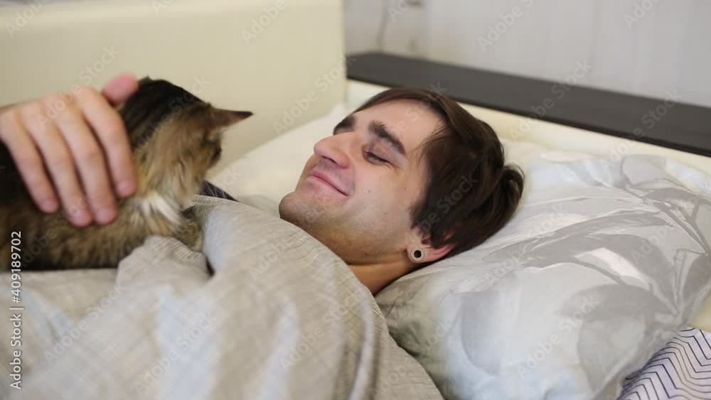 The cat wakes up the man of its owner with a paw, asleep in bed
