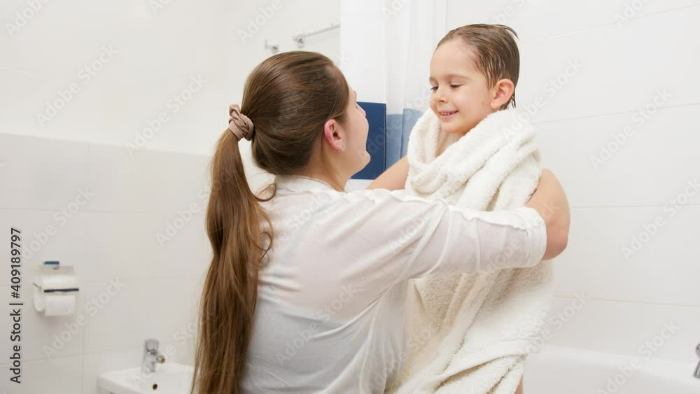 Young caring mother wiping and drying her little son with white towel after washing in bath. Concept of child hygiene and health care at home. Young caring mother wiping and drying her little son with white towel after washing in bath. Concept of child hygiene and health care at home.