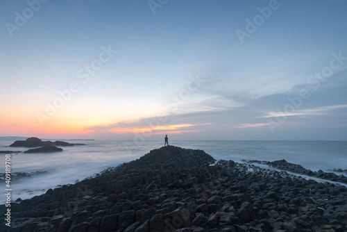 Sunrise scenery with a man standing on the edge of basalt pillars by the sea in Zhangzhou Volcano Geopark