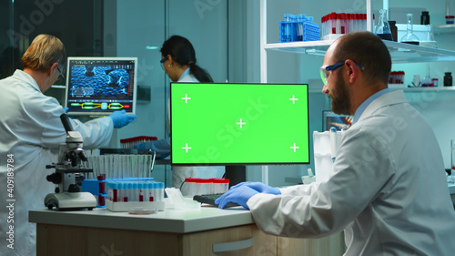 Man researcher looking at chroma key computer in modern equipped lab working overtime. Team of microbiologists doing vaccine research writing on device with green screen, isolated, mockup display.