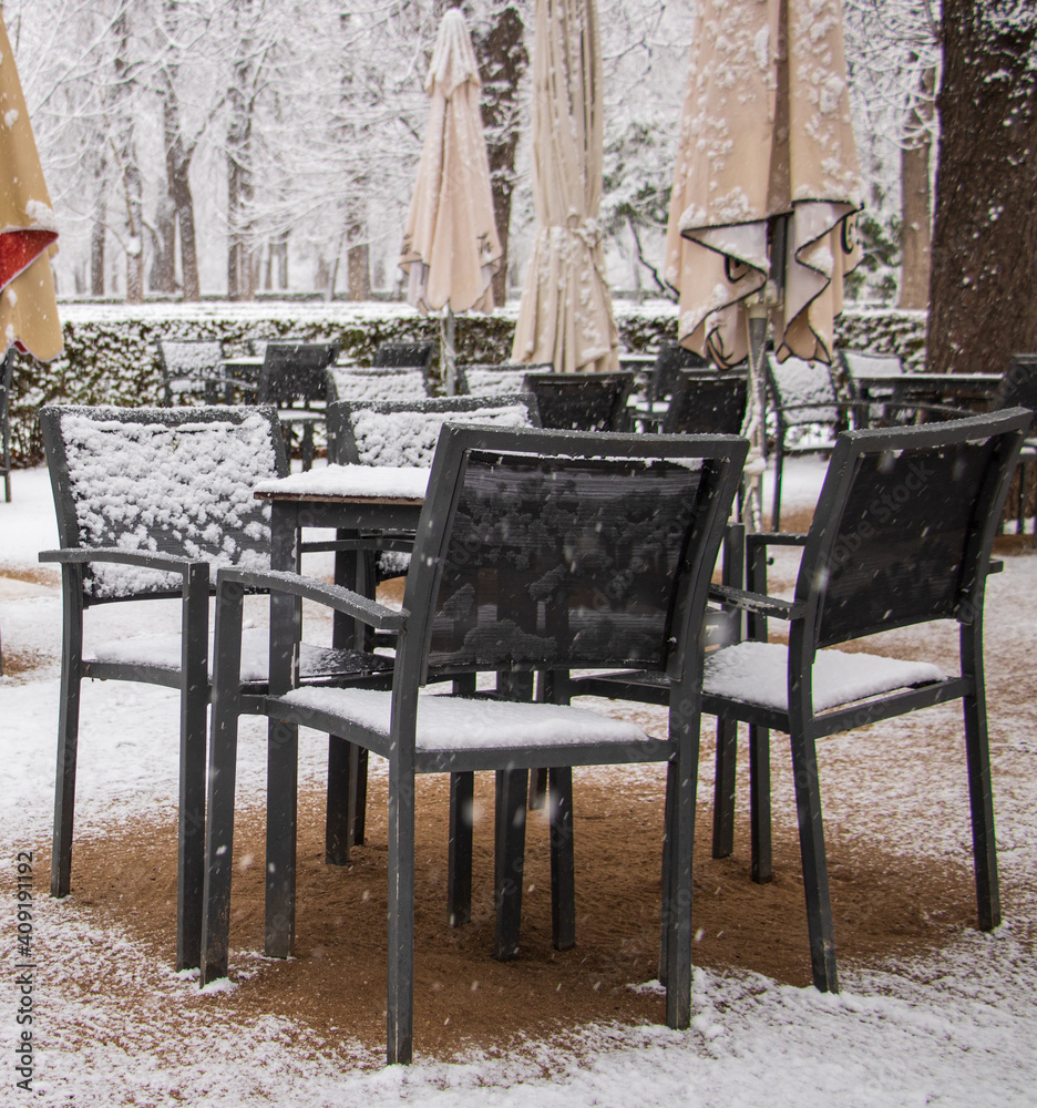 Naklejka premium tables and chairs on a terrace of an empty restaurant with no client because of virus and snowstorm in garden with umbrellas