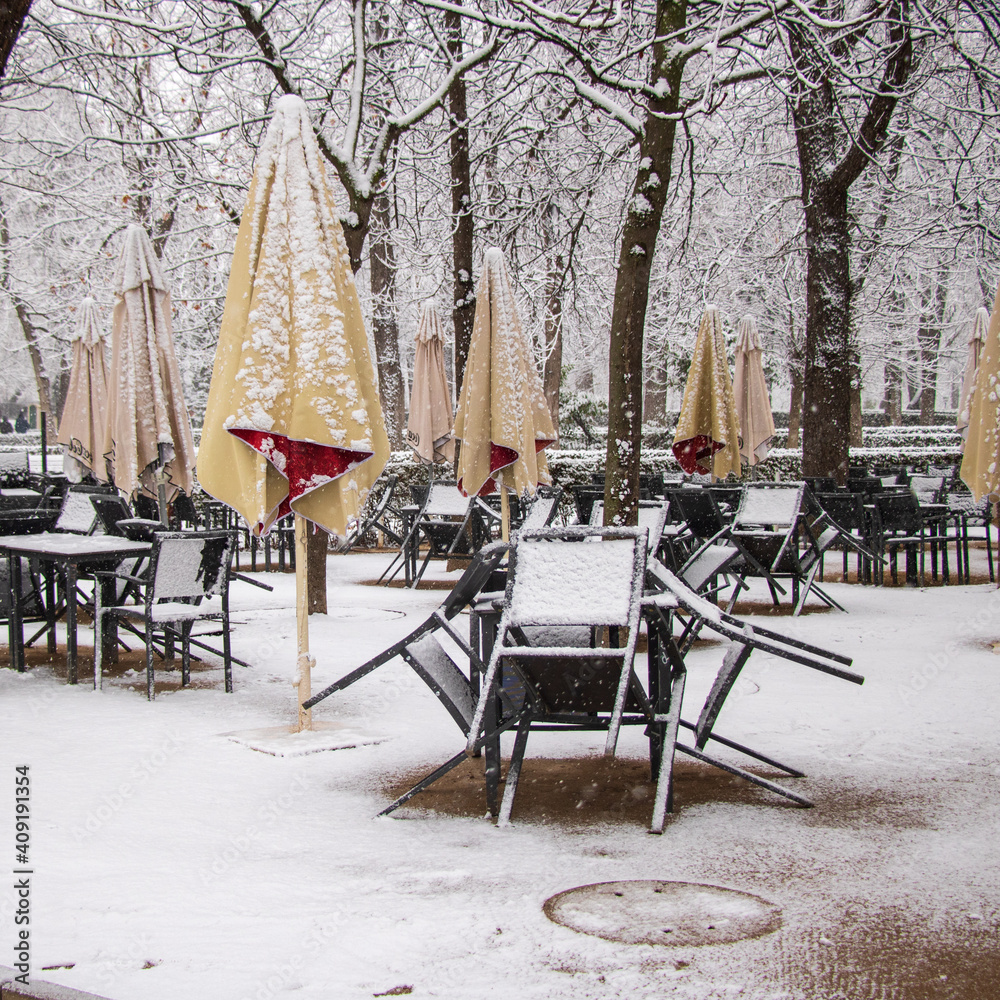 Obraz premium tables and chairs on a terrace of an empty restaurant with no client because of virus and snowstorm in garden with umbrellas