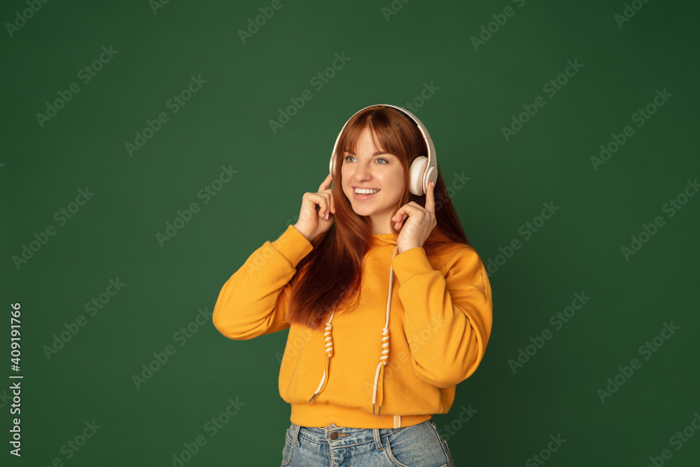 Joyful. Caucasian woman's portrait isolated on green studio background with copyspace. Beautiful female model with headphones. Concept of human emotions, facial expression, sales, ad, fashion. Joyful. Caucasian woman's portrait isolated on green studio background with copyspace. Beautiful female model with headphones. Concept of human emotions, facial expression, sales, ad, fashion.
