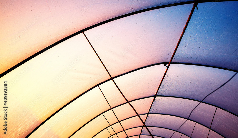 Plastic greenhouse cover with rusty frame at sunset, abstract industrial background. - obrazy, fototapety, plakaty 