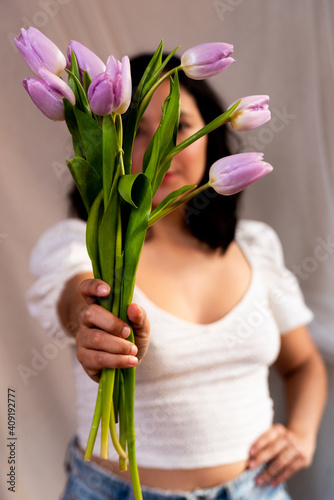 young woman holding lilac tulips with natural soft light and casual informal dress. concept of spring time and femininity. authentic people, natural looking portrait and lifestyle