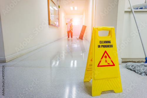 caution wet floor warning sign with blurred worker mopping floor