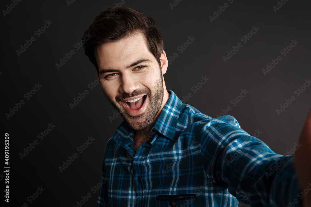 Joyful handsome unshaven guy smiling while taking selfie
