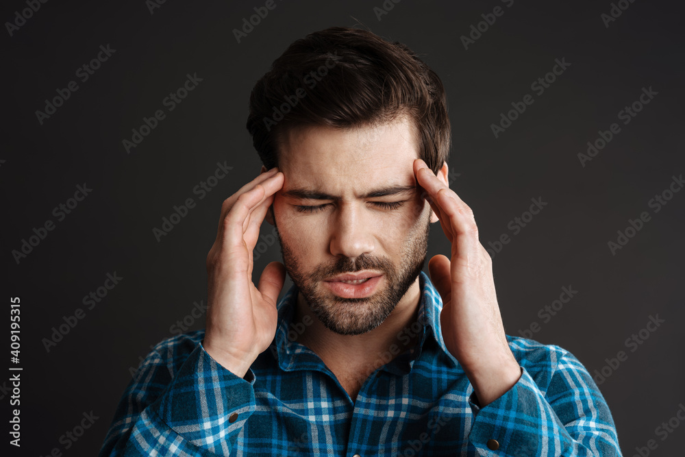 Unhappy handsome unshaven guy with headache rubbing his temples