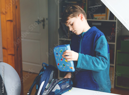 School kid boy getting ready in the morning for school. Healthy child filling satchel with books, pens, folders and school stuff. Preaparation, routine concept. photo