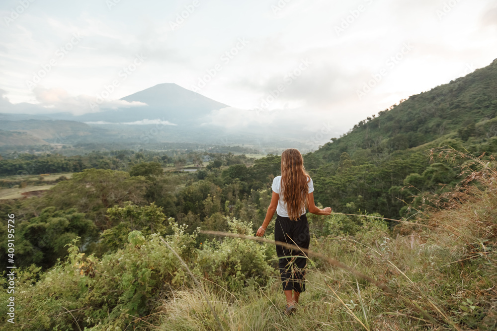 Rear view female tourist enjoying nature looking at the mountains and Agung volcano during her trip on Bali island