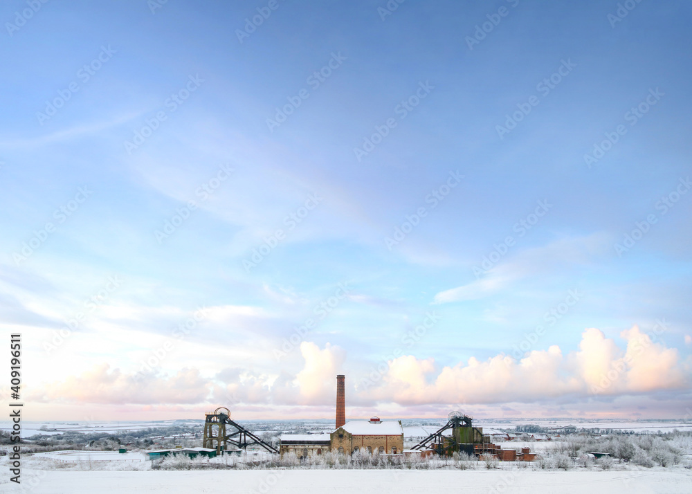 Old abandoned national coal board mine in countryside with industry engine house and winding wheels after snowfall Christmas winter scene landscape beautiful sky
