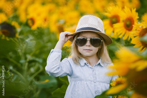 Little girl of six years old poses for the camera in a field of sunflowers  laughs and holds a hat in her hands