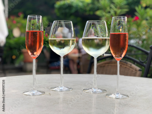 Four glasses with wine. Two glasses of rose wine and white wine on table in outdoor restaurant in summer.