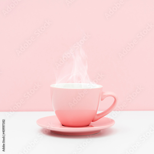 Pink cup with steam, coffee or tea on pink background.