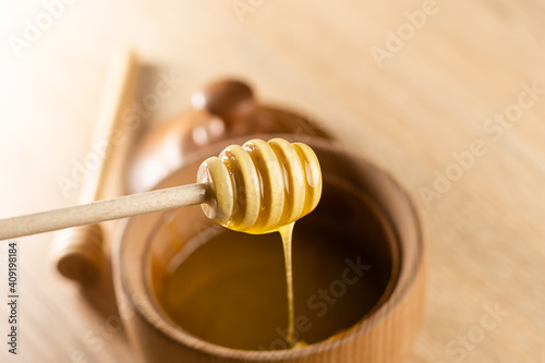 honey in a deep wooden bowl, rustic wooden plate. The wooden spoon drips slowly.