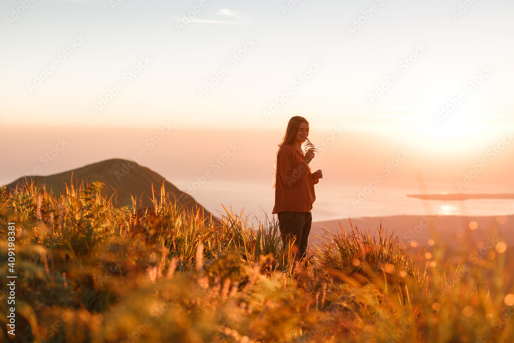 Carefree happy woman in sweater enjoying nature on grass meadow on top of mountain with sunrise. Beauty girl outdoor with sunbeams. Freedom concept
