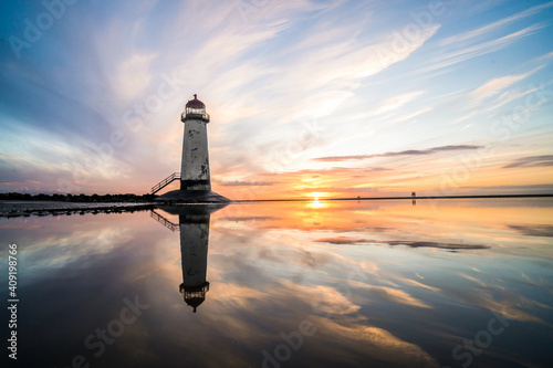 Lighthouse standing in pool of water stunning sunset sunrise reflection reflected in water and sea steps up to building north Wales seashore sand beach still water orange glow golden hour blue hour