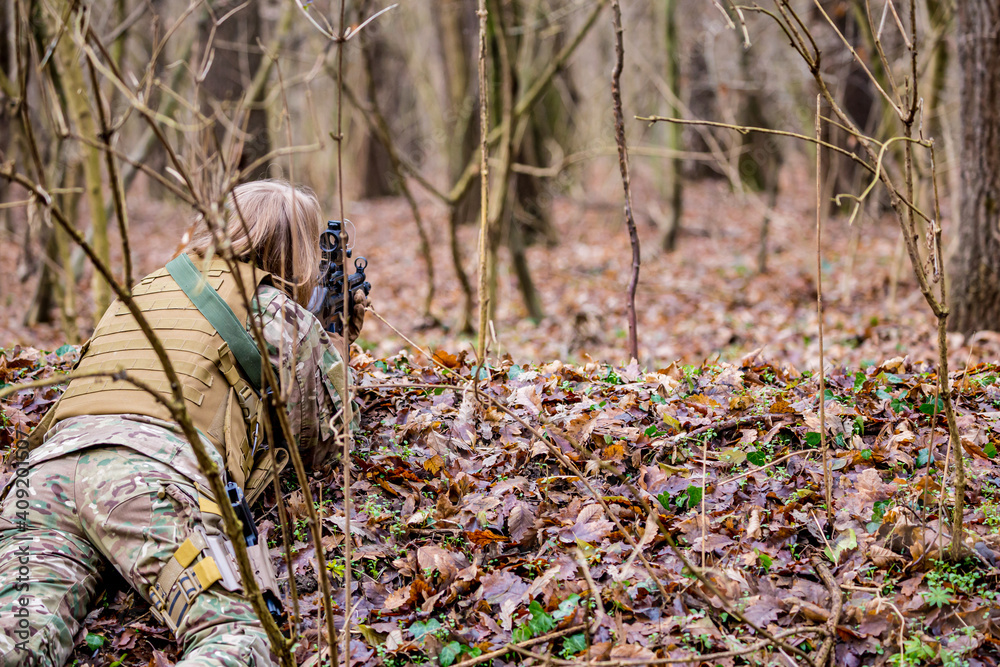 Obraz premium Beautiful girl in military uniform with an airsoft gun lying on the ground in the forest