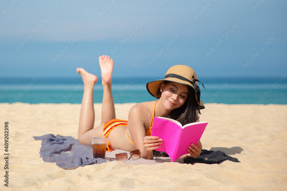 An Asian woman takes A rest and reading a pink book on the beach While relaxing on vacation for the weekend on sunny days and nice weather in travel and holiday concept.