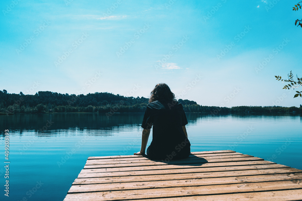 girl sitting on the edge of Banyoles lake with the landscape reflected in the water girl sitting on the edge of Banyoles lake with the landscape reflected in the water