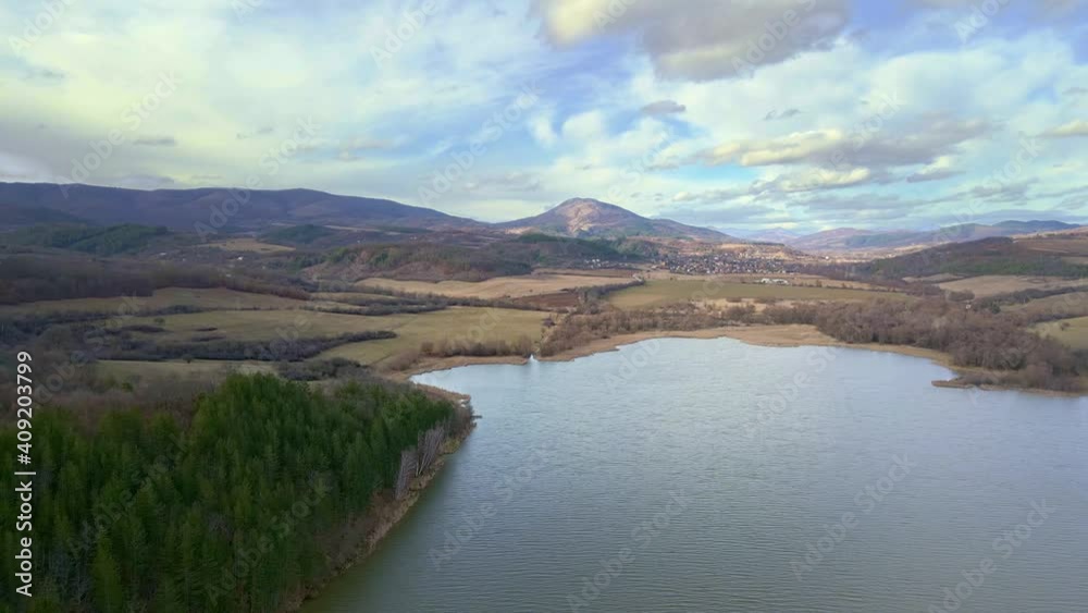 Aerial view of green forest, beautiful lake. Drone flight over a green pine forest. Late winter natural landscape. Fields, mountains and beautiful cloudy sky as a background. Aerial view of green forest, beautiful lake. Drone flight over a green pine forest. Late winter natural landscape. Fields, mountains and beautiful cloudy sky as a background.