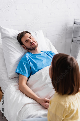 girl holding hand of sick father frowning while lying with hospital bed with closed eyes photo