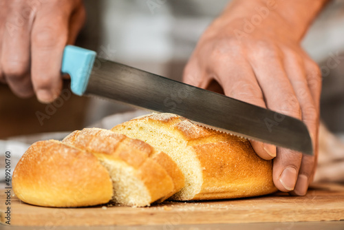 A man cuts bread with a serrated knife.