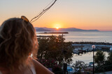 Nea Hora marina beach in Chania, Crete, Grece. Traditional greek tavern by the sea. Boats anchoring at the marina. Romantic sunset, warm colors. Girl with blond curly long hair look towards horizon.