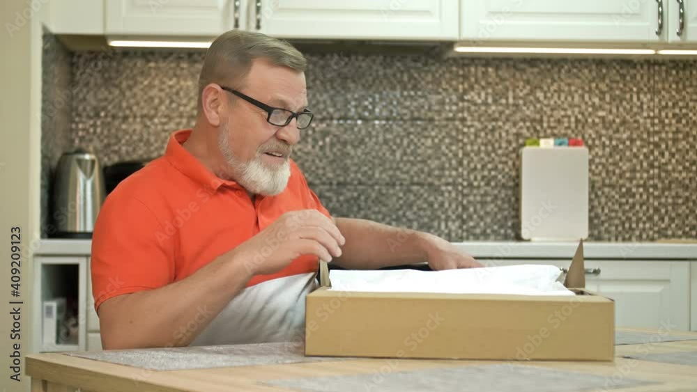 Happy elderly man unpacks a parcel. A satisfied regular customer of the courier delivery service. Online shopping. Happy elderly man unpacks a parcel. A satisfied regular customer of the courier delivery service. Online shopping.
