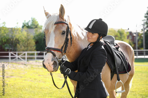 Young woman in horse riding suit and her beautiful pet outdoors on sunny day