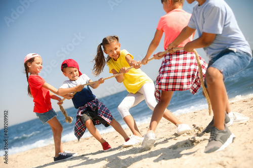 Cute children pulling rope during tug of war game on beach. Summer camp photo