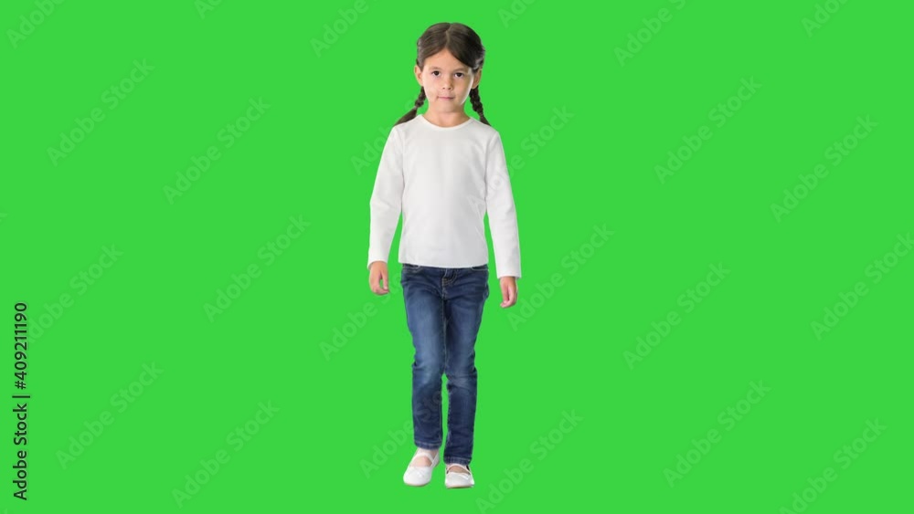 Little girl with pig tails dressed in white long sleeve top and jeans walking and looking at camera on a Green Screen, Chroma Key. Little girl with pig tails dressed in white long sleeve top and jeans walking and looking at camera on a Green Screen, Chroma Key.