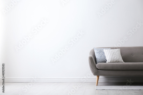 Grey sofa with pillows near white wall in stylish living room interior. Space for text