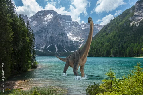 Obraz Brachiosaurus walks alone into cold lake before dinosaurs extinction. Snow on the mountains in the background.