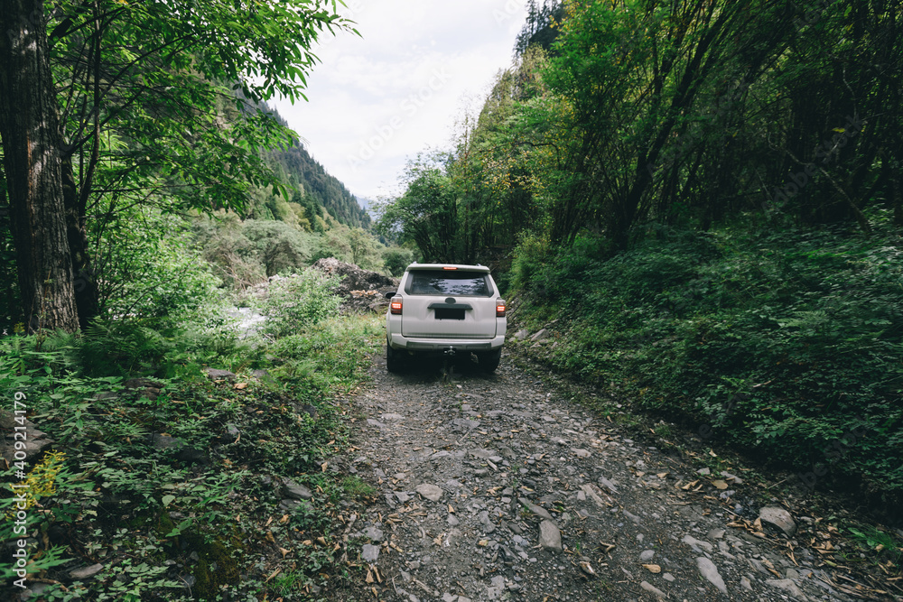 Driving offroad car on trail in high altitude forest mountain