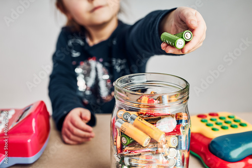 Little girl putting used batteries into jar for recycling. Child separating waste. Batteries only container photo