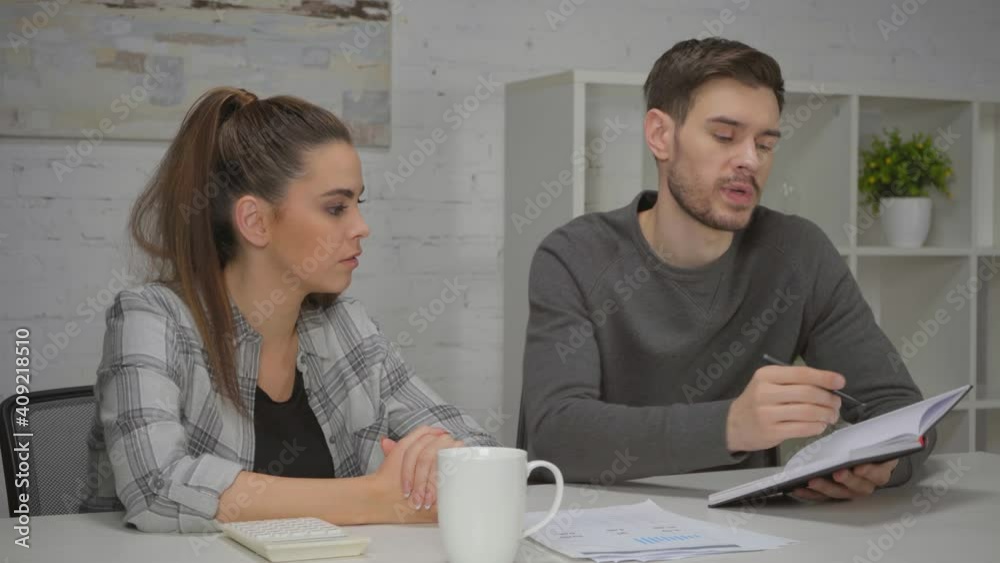man flipping pages of notebook while talking with woman at home