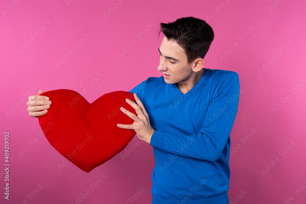A young guy holds a heart in his hands. Valentine's Day. Pink background. A young guy holds a heart in his hands. Valentine's Day. Pink background.