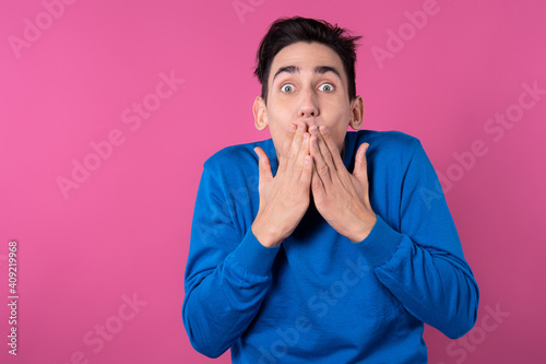The young man is surprised. Pink background. Blue clothes.