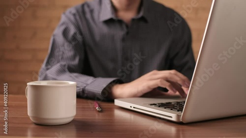 Close-up view of man using laptop and holding white cup