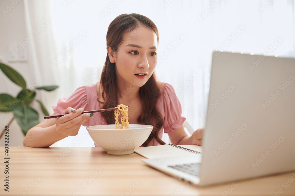 Portrait of young Asian girl using laptop while eating noodles at home. Portrait of young Asian girl using laptop while eating noodles at home.