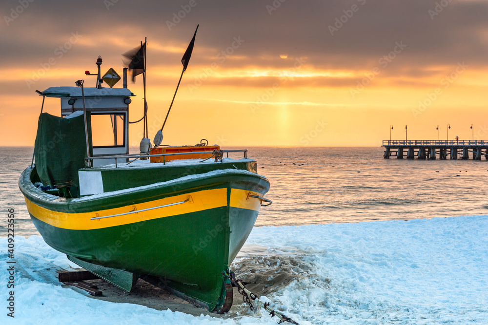 Fishing boat on snowy beach in Gdynia Orlowo at sunrise, Baltic Sea. Poland.